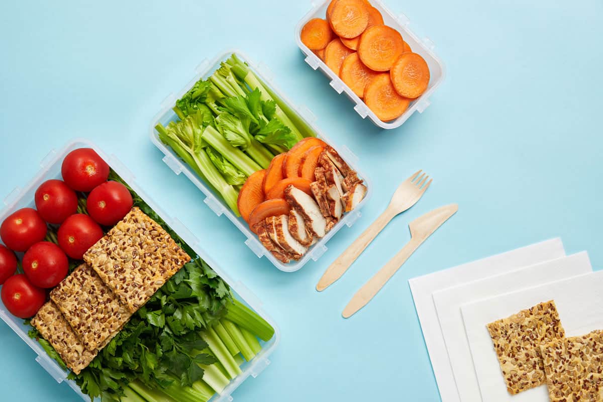 不同的蔬菜放在塑料容器里，旁边放着纸巾和其他塑料容器，塑料食物容器可以放在洗碗机里吗?”width=
