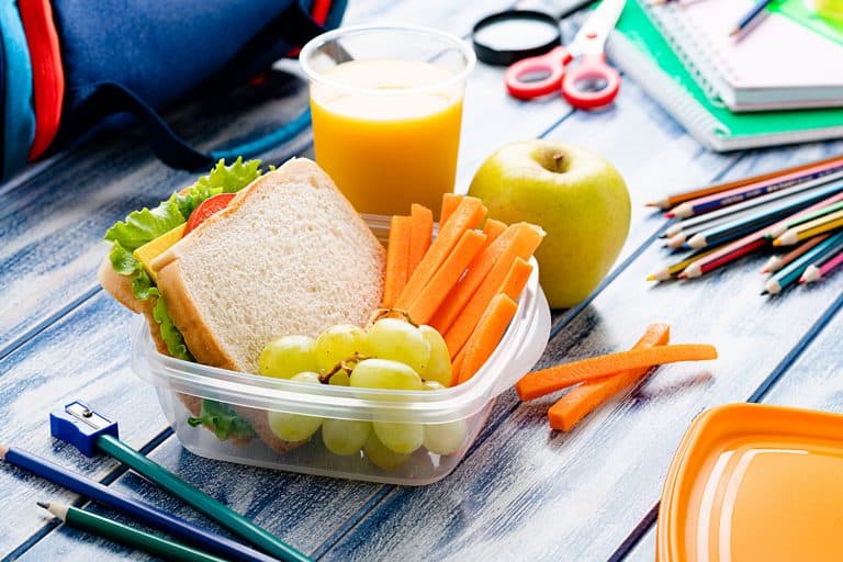 对孩子健康食品的概念:均衡的学校午餐盒蓝色的桌子上。学校供应的午餐盒,如何密封塑料食品容器(4酷技巧!)