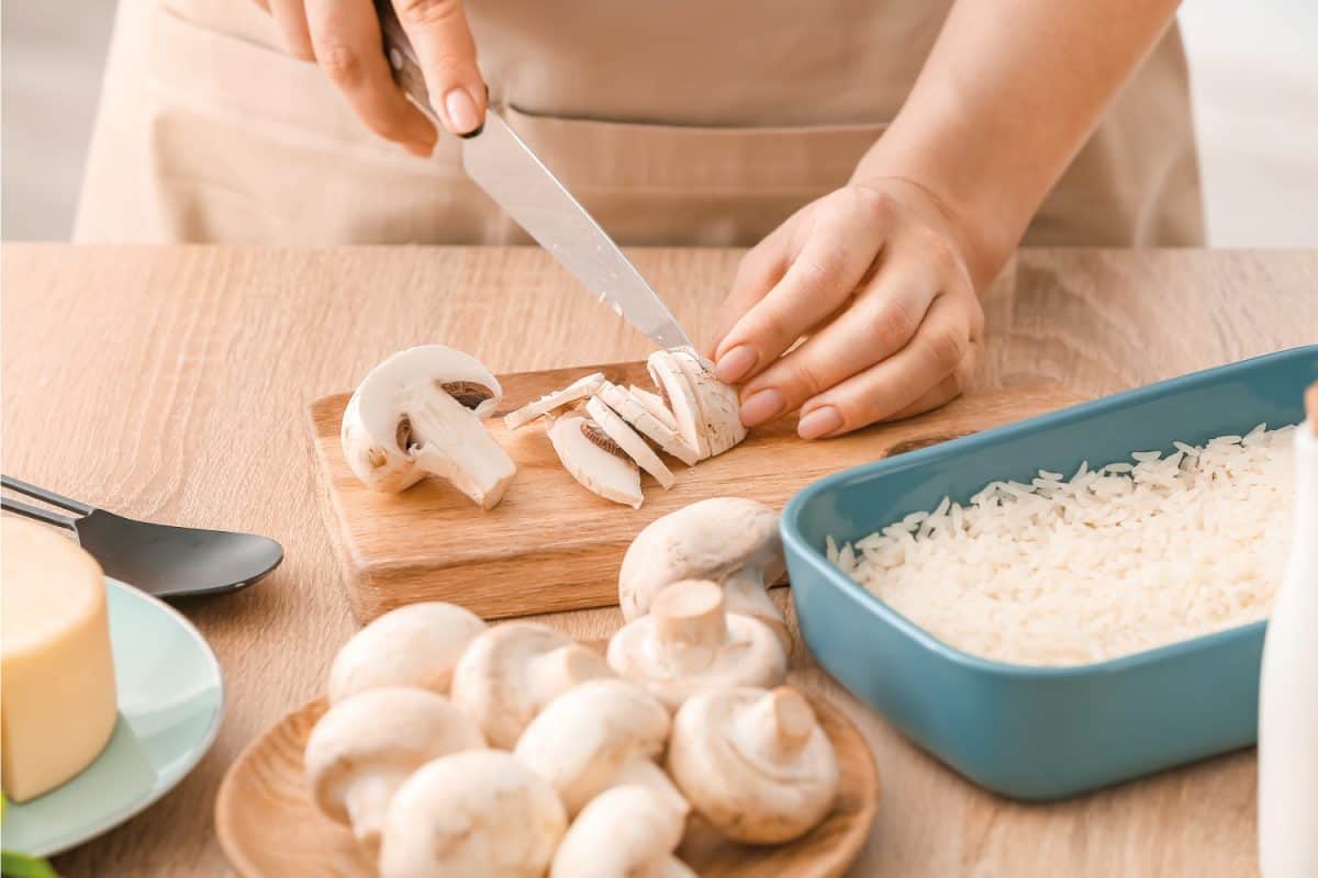 女人在桌子上煮砂锅饭，在菜板上切蘑菇