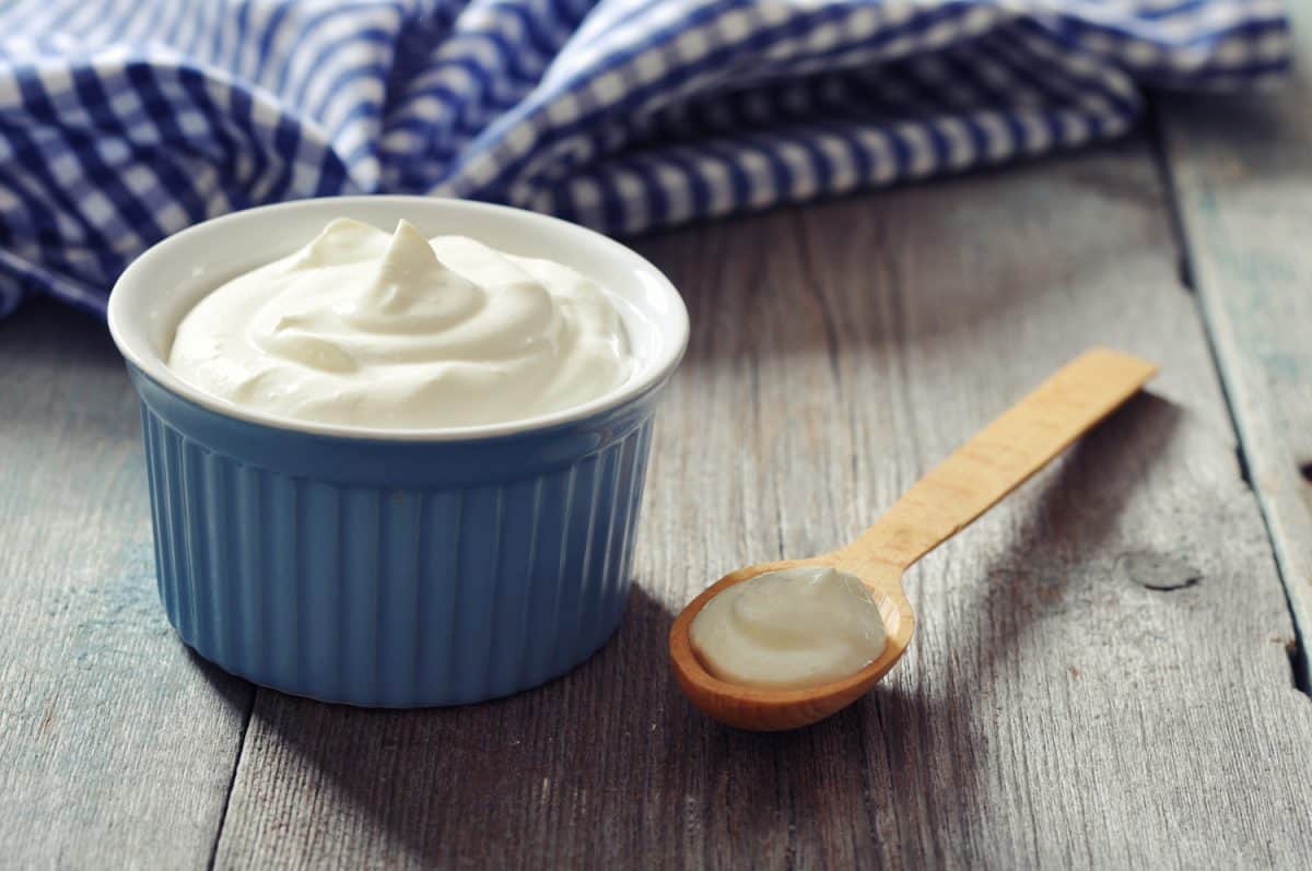 希腊酸奶放在陶瓷碗里，勺子放在木制背景上