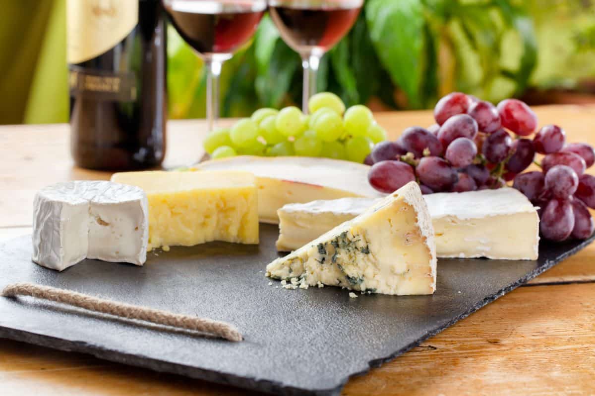 案板上放着不同的奶酪片，旁边放着葡萄和葡萄酒