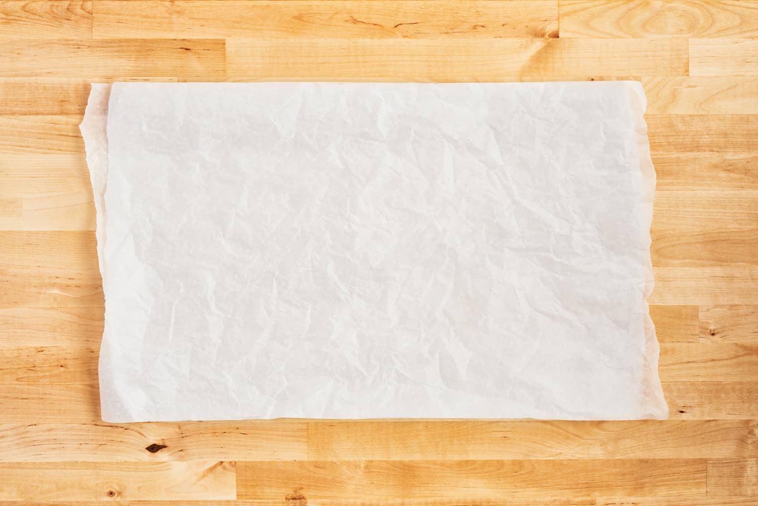将揉皱的白色羊皮纸或烤纸放在木桌上。前视图。