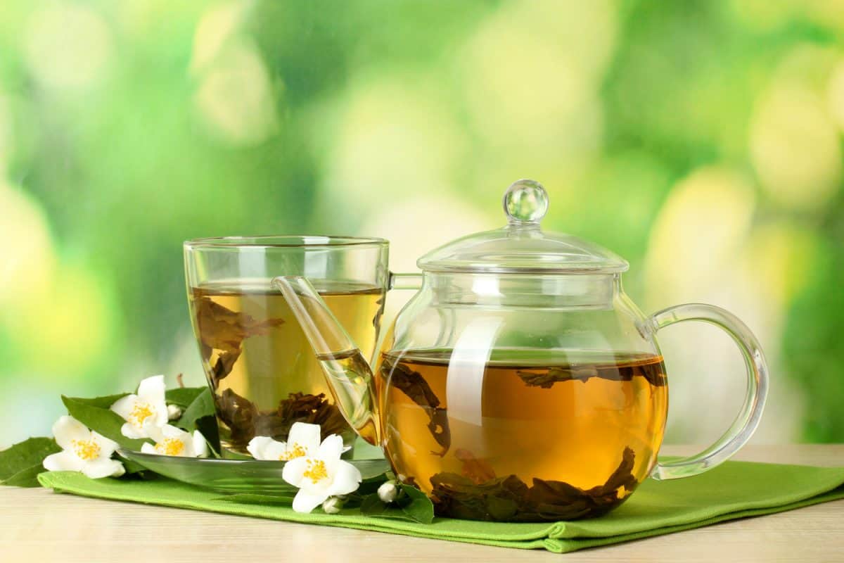 绿茶和茉莉花在茶杯和茶壶在绿色背景的木桌上