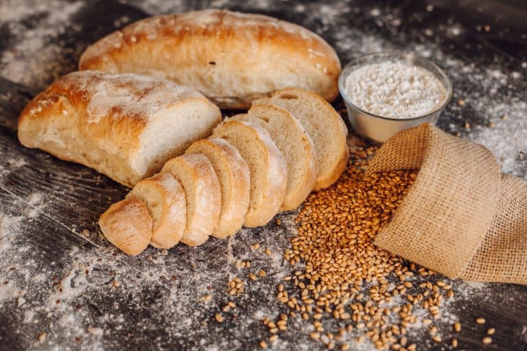 自制的面包在桌子上,旁边一袋谷物和一碗面粉,如何没有面包刀切面包