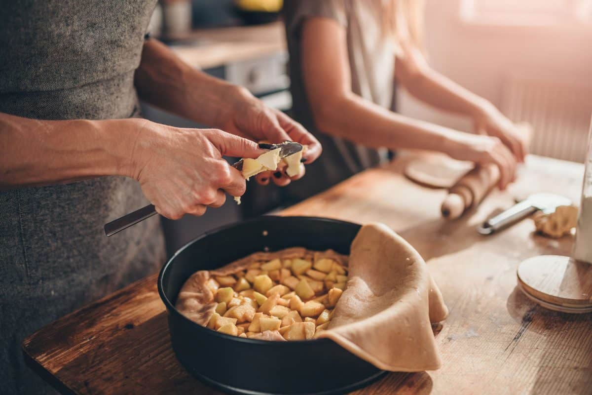 一个女人站在厨房的木桌旁，把黄油切成苹果派bd手机下载
