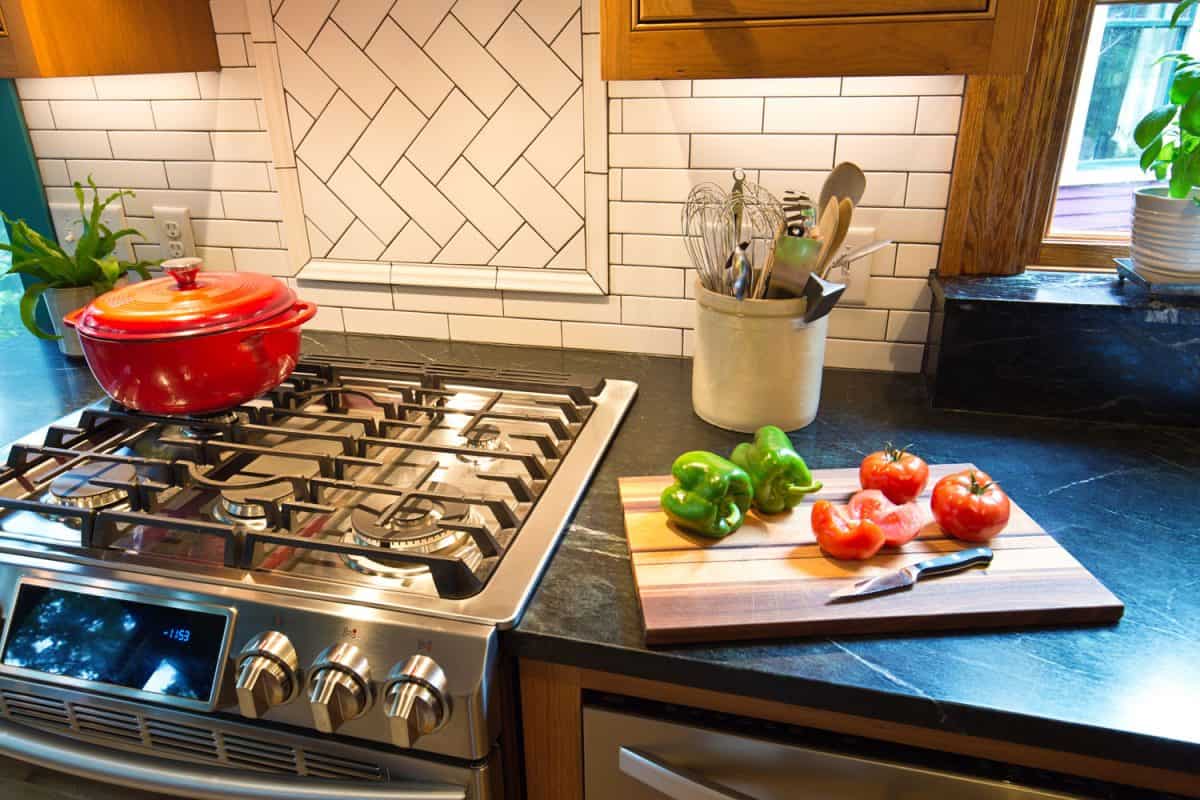这是一个经典风格的厨房，灶台上有一bd手机下载个橙色的荷兰烤箱，案板上有柿子椒