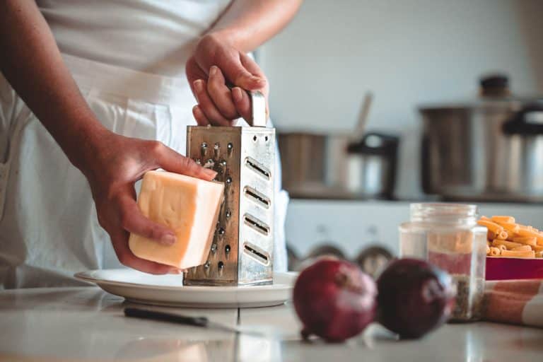 一个女人光栅奶酪在她厨房的意大利面,你应该买碎奶酪或炉篦自己的吗?bd手机下载