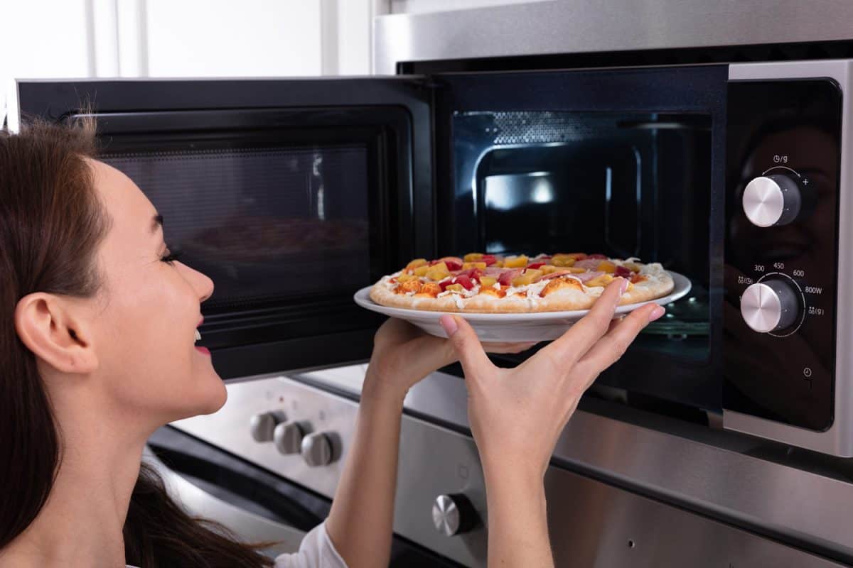 一个快乐的女人在微波炉里烤披萨的特写