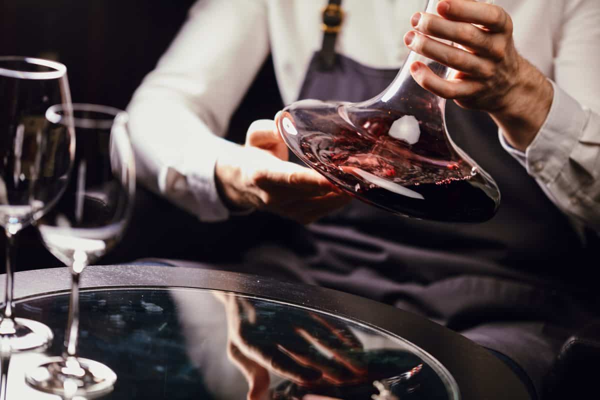 在葡萄酒餐厅的桌子上，专业侍酒师手持混合碗和红酒的裁剪视图。