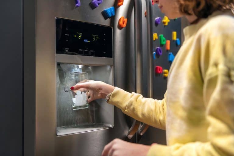 女孩用冰从电冰箱冰填充玻璃制造商,如何重置电冰箱制冰机