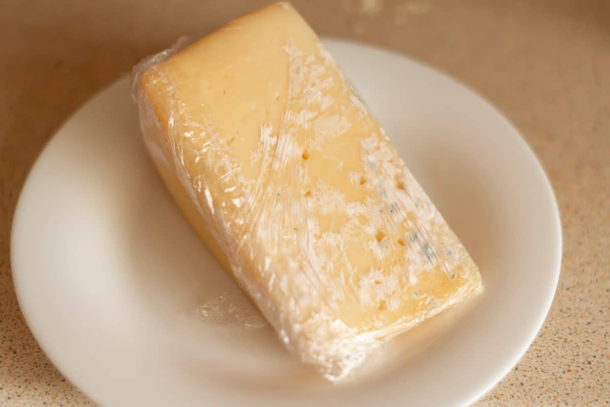 用保鲜膜包裹着发霉的奶酪。不正确的储存，变质的产品，过期的概念。