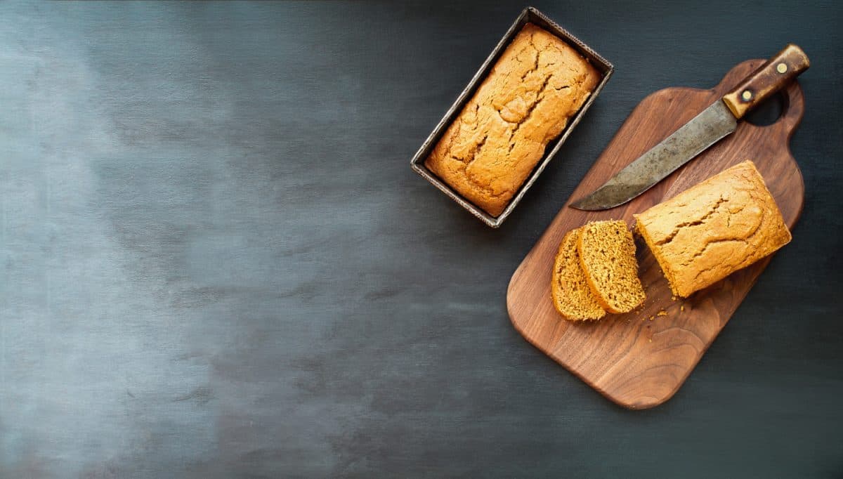 两个刚烤好的自制南瓜面包，黑色背景上有刀。图像拍摄从顶视图，平。
