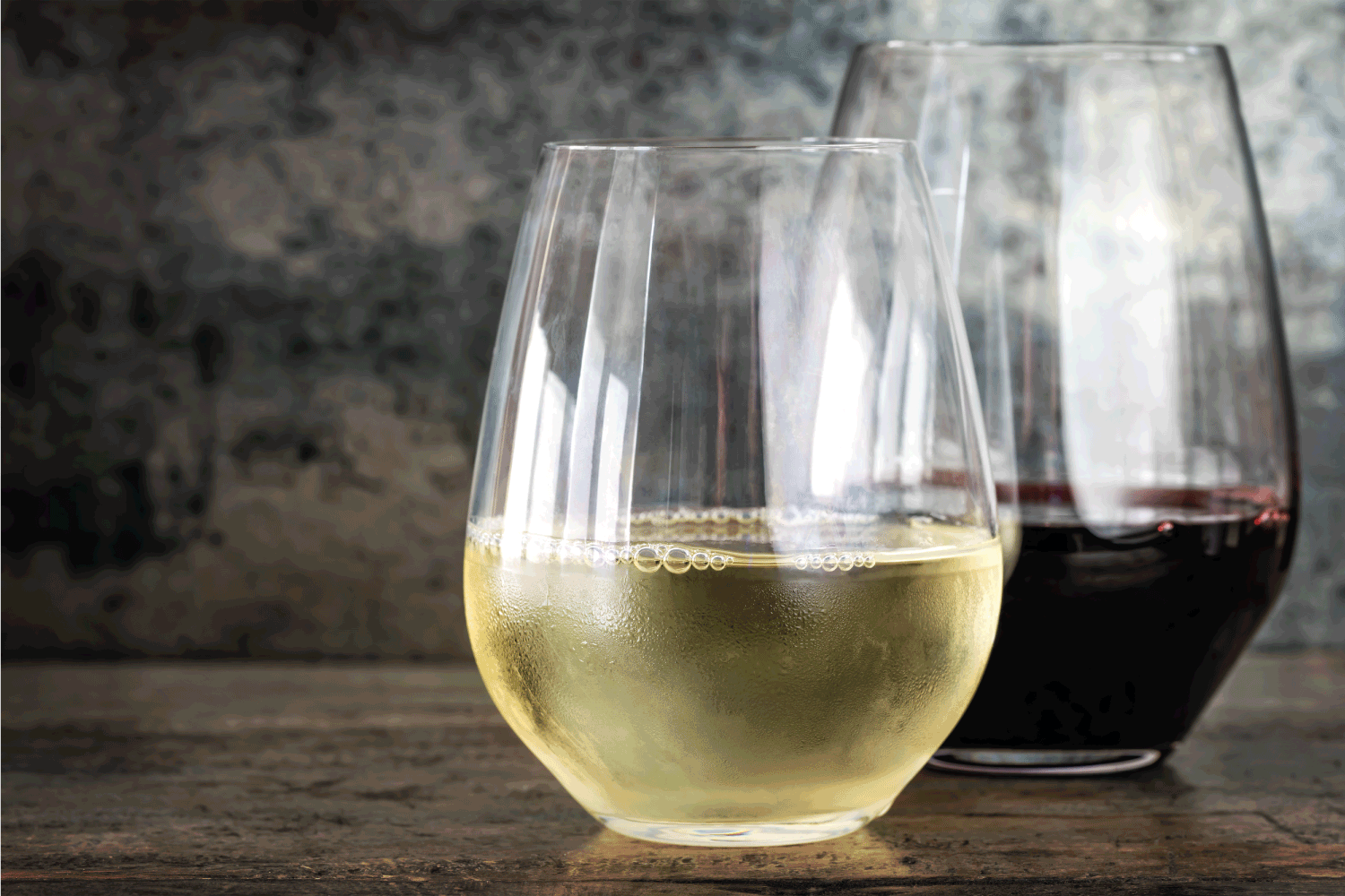 白葡萄酒和红葡萄酒，现代无茎玻璃杯，石板和木材背景