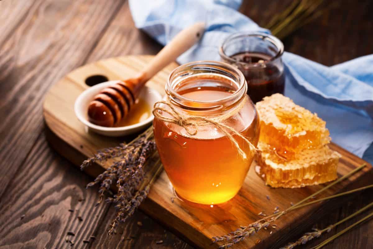 一罐液体蜂蜜，里面有蜂巢，旧木桌上放着一束干薰衣草。深色乡村风格，选择性聚焦