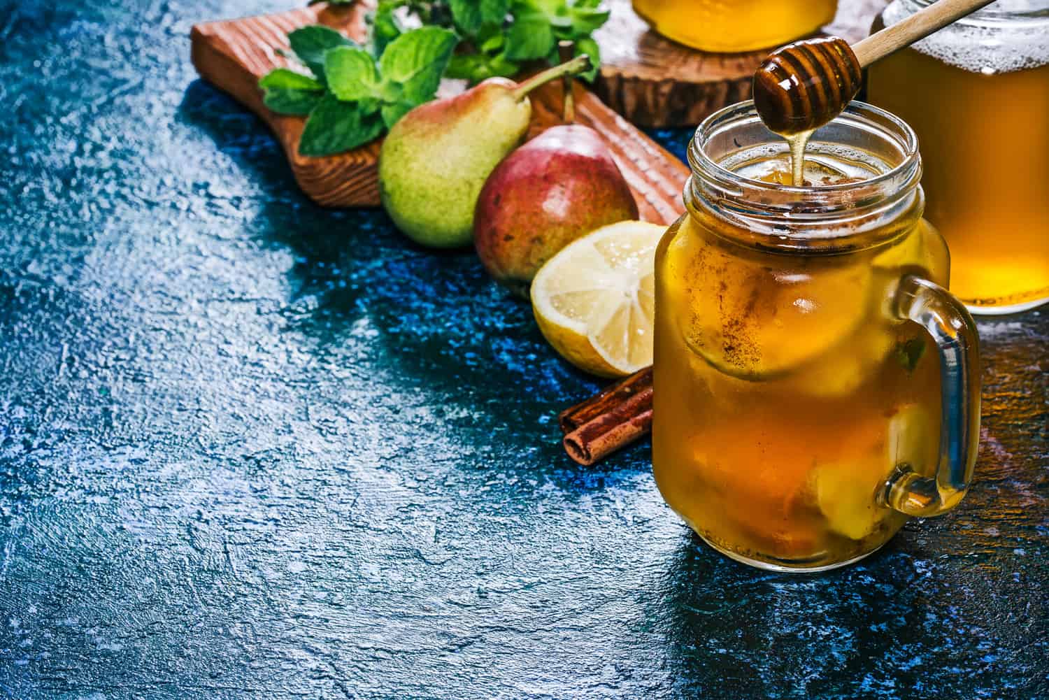 桑格利亚汽酒梨苹果酒，新鲜的梨和柠檬，蜂蜜和肉桂在梅森罐与材料。蓝色背景。