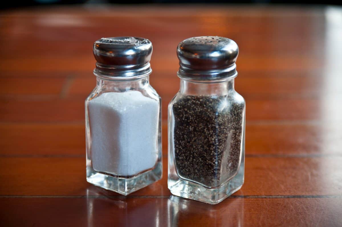 一对简单的玻璃盐和胡椒瓶单独放在一个清漆的木制桌面上。