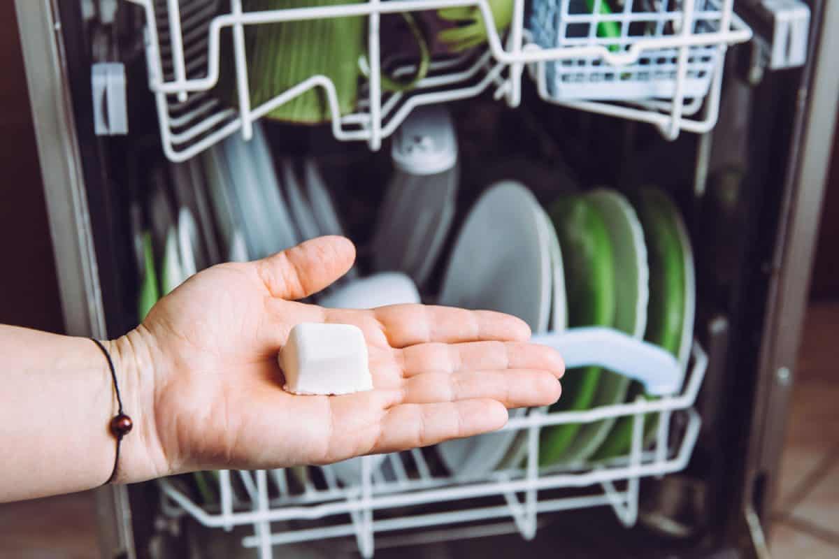 选择性聚焦在女人的手，拿着自制的自然洗碗机pod散焦盘子在洗碗机的背景