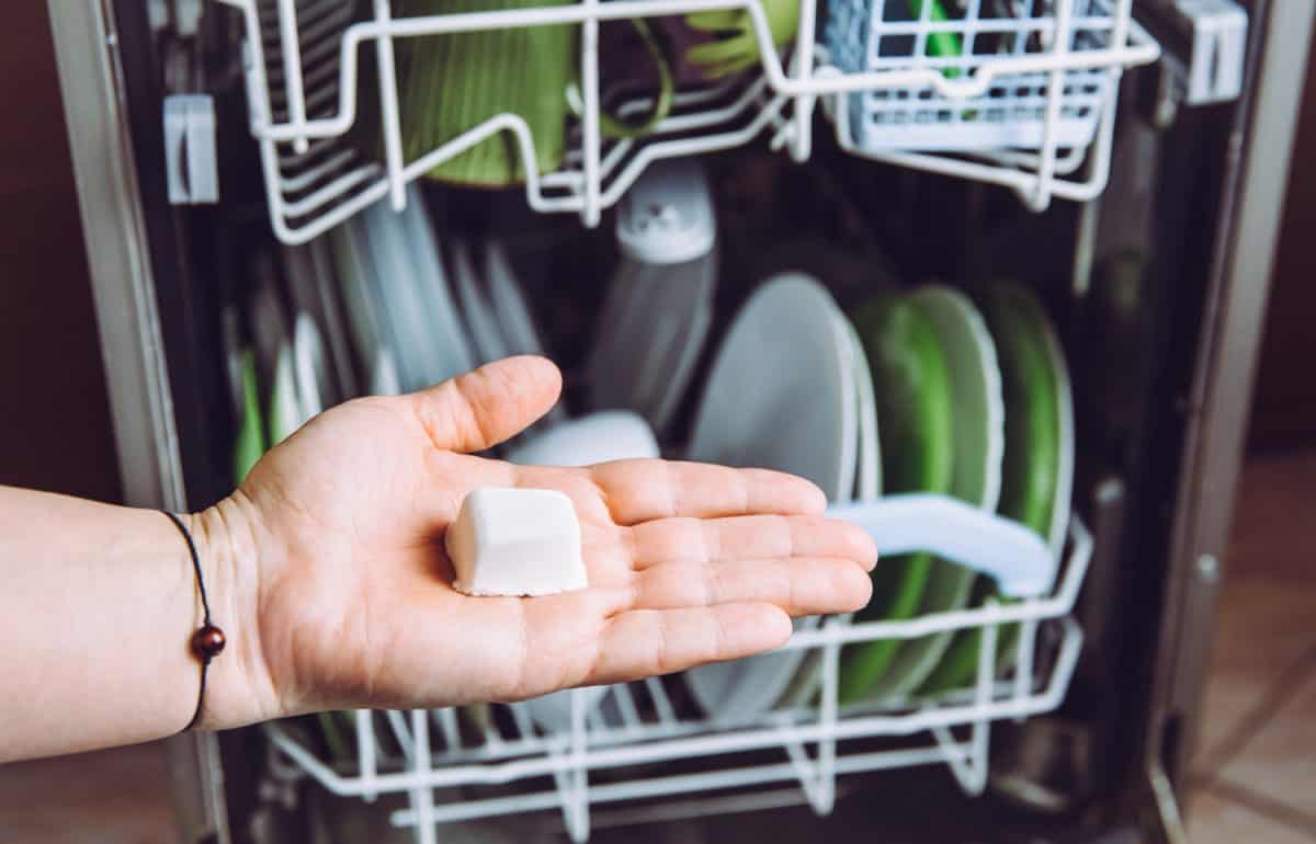 选择性聚焦在女人的手，拿着自制的自然洗碗机pod散焦盘子在洗碗机的背景。绿色可持续的生活理念。