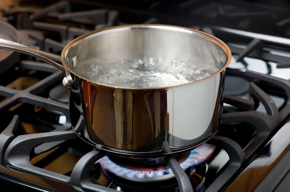 水在家庭厨房的煤气炉或炉灶上起泡沸腾。bd手机下载蓝色火焰和不锈钢锅。＂width=