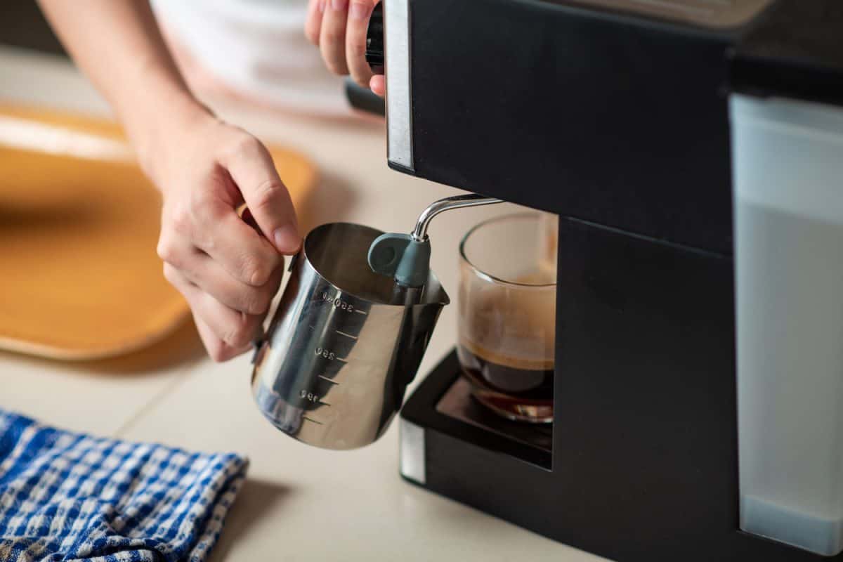 一个女人从浓缩咖啡机里倒出蒸牛奶，来泡一杯舒缓的咖啡