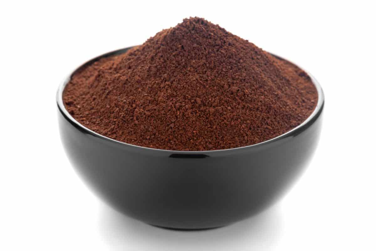 特写的有机深棕色咖啡颗粒在白色背景黑色陶瓷碗