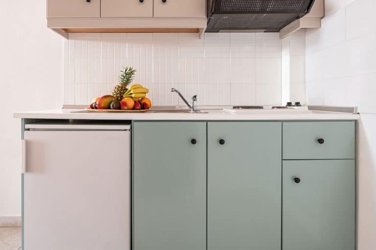在现代室内厨房的简单橱柜模块的空墙上的白色瓷砖防溅特写，带小冰箱，通风口，水槽，炉子，水果盘，如何反转丹比冰箱上的门bd手机下载
