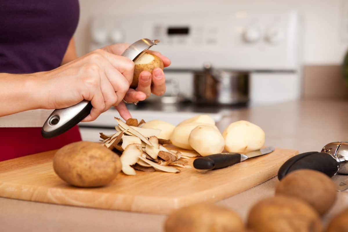 彩色图像的一个年轻女人剥马铃薯在她家的厨房里。bd手机下载