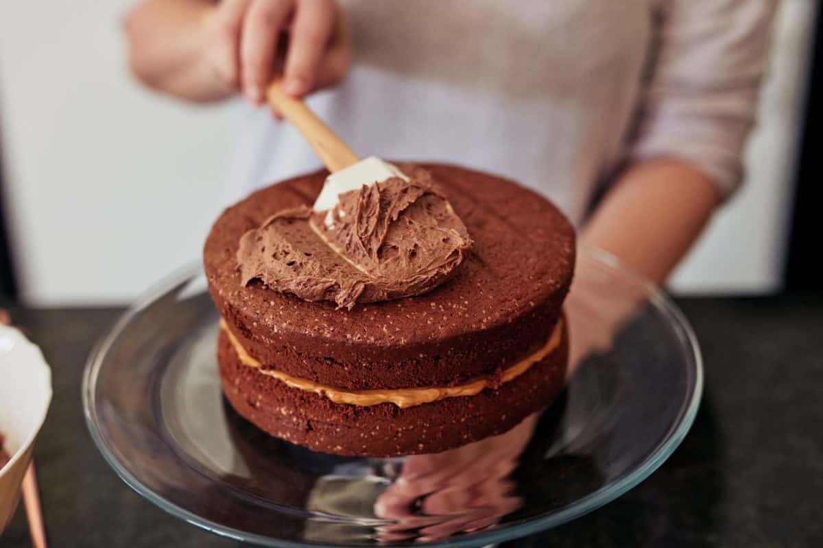 一个面目全非的女人在家里把奶油抹在刚烤好的巧克力蛋糕上
