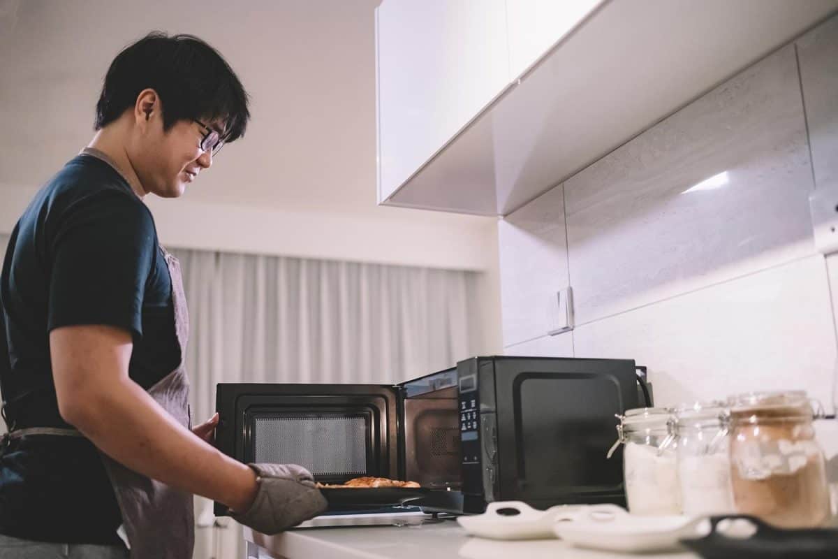 一个亚洲中国男性在披萨从微波炉在厨房手套bd手机下载