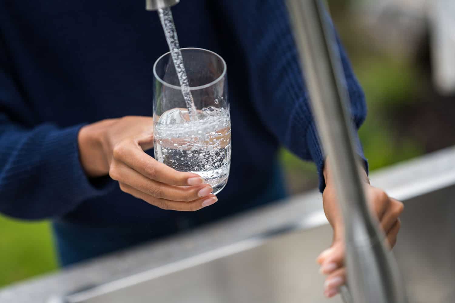 在花园水槽里，女人的手往玻璃杯里注水的特写镜头。