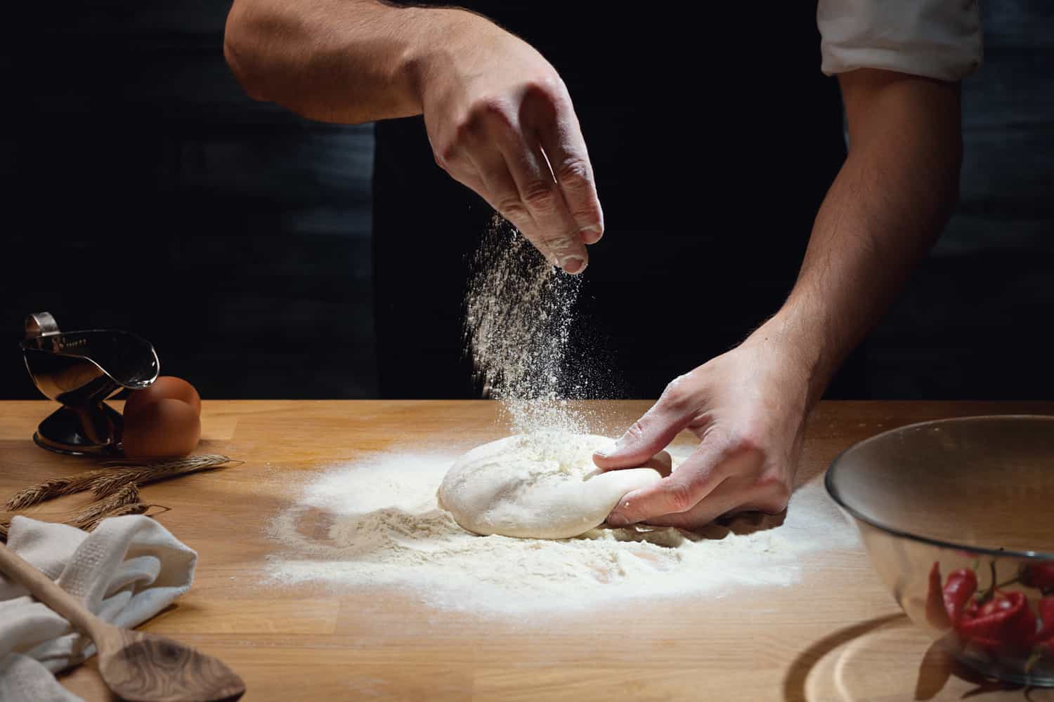 Cook hands kneading dough, sprinkling piece of dough with white wheat flour.