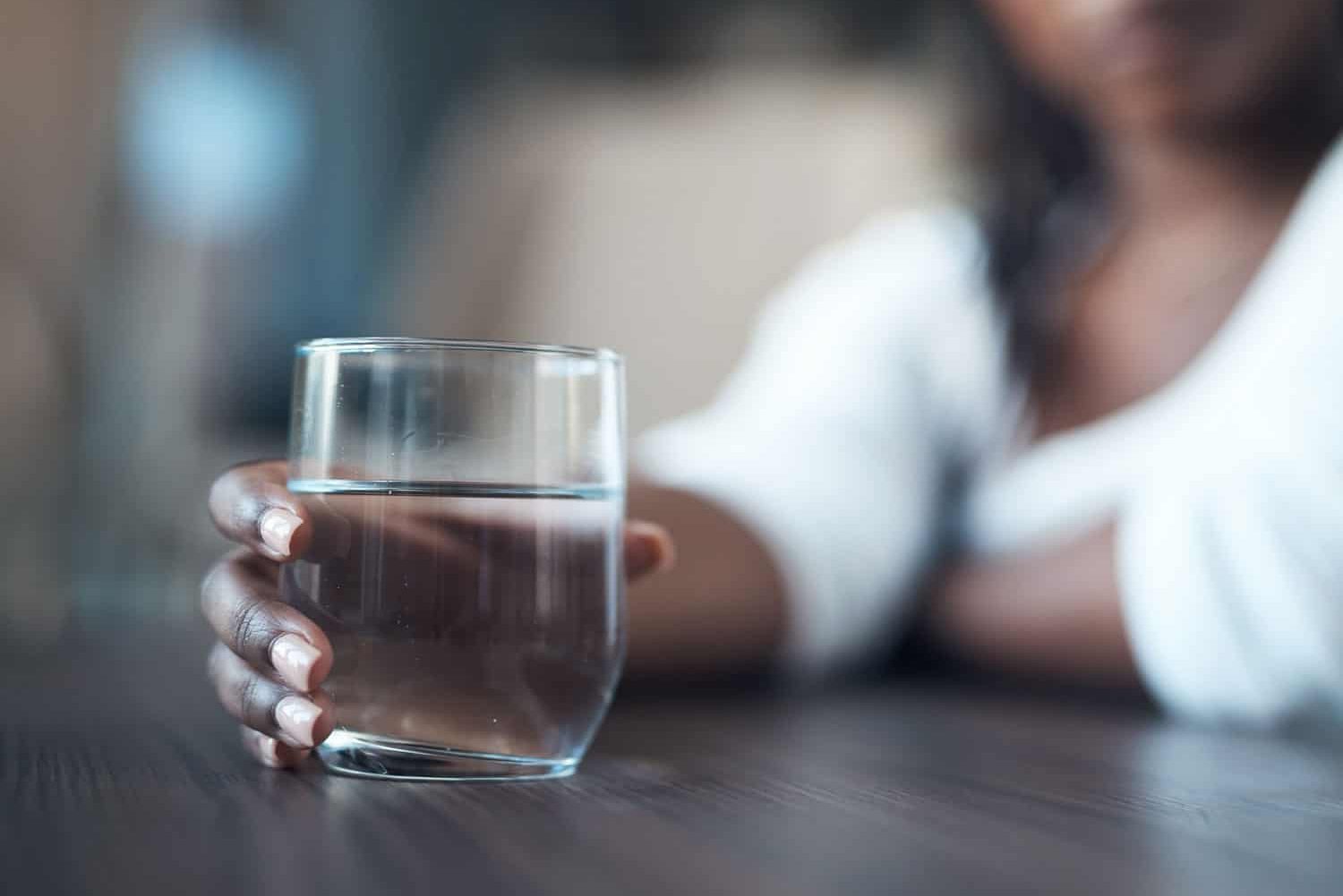 一个迷人的年轻女子独自坐在家里，拿着一杯水