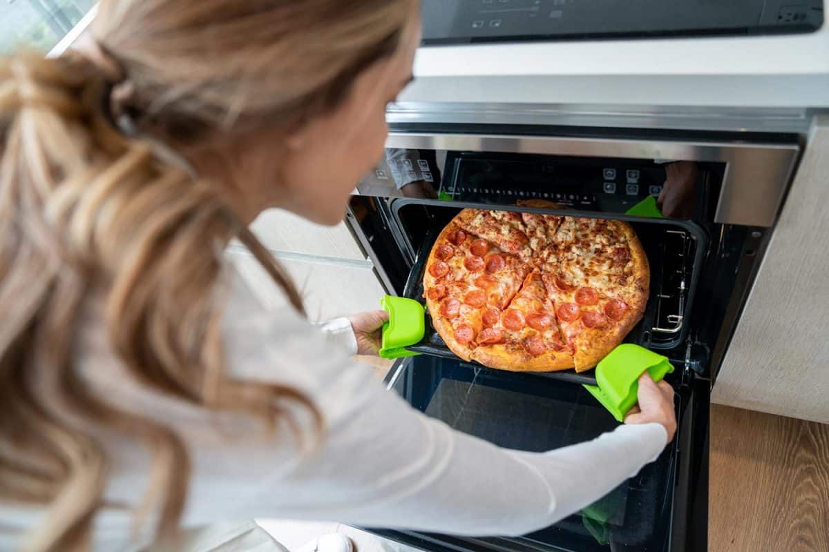 高角度视图面目全非的妇女从烤箱取出一个新鲜的烤披萨在家里