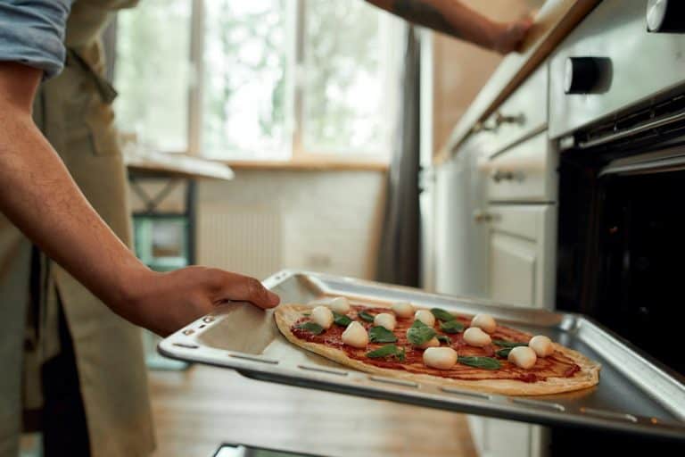 一名男子围裙把生在现代烤箱烤披萨,做比萨烤箱里多久?