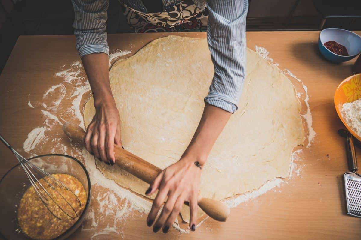 面包师用擀面杖揉面团制作手工卷的照片