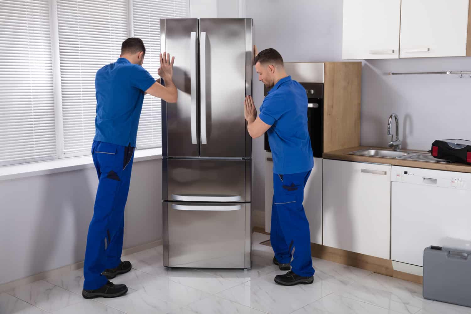 两个年轻的男性搬运工在厨房里放置钢制冰箱bd手机下载