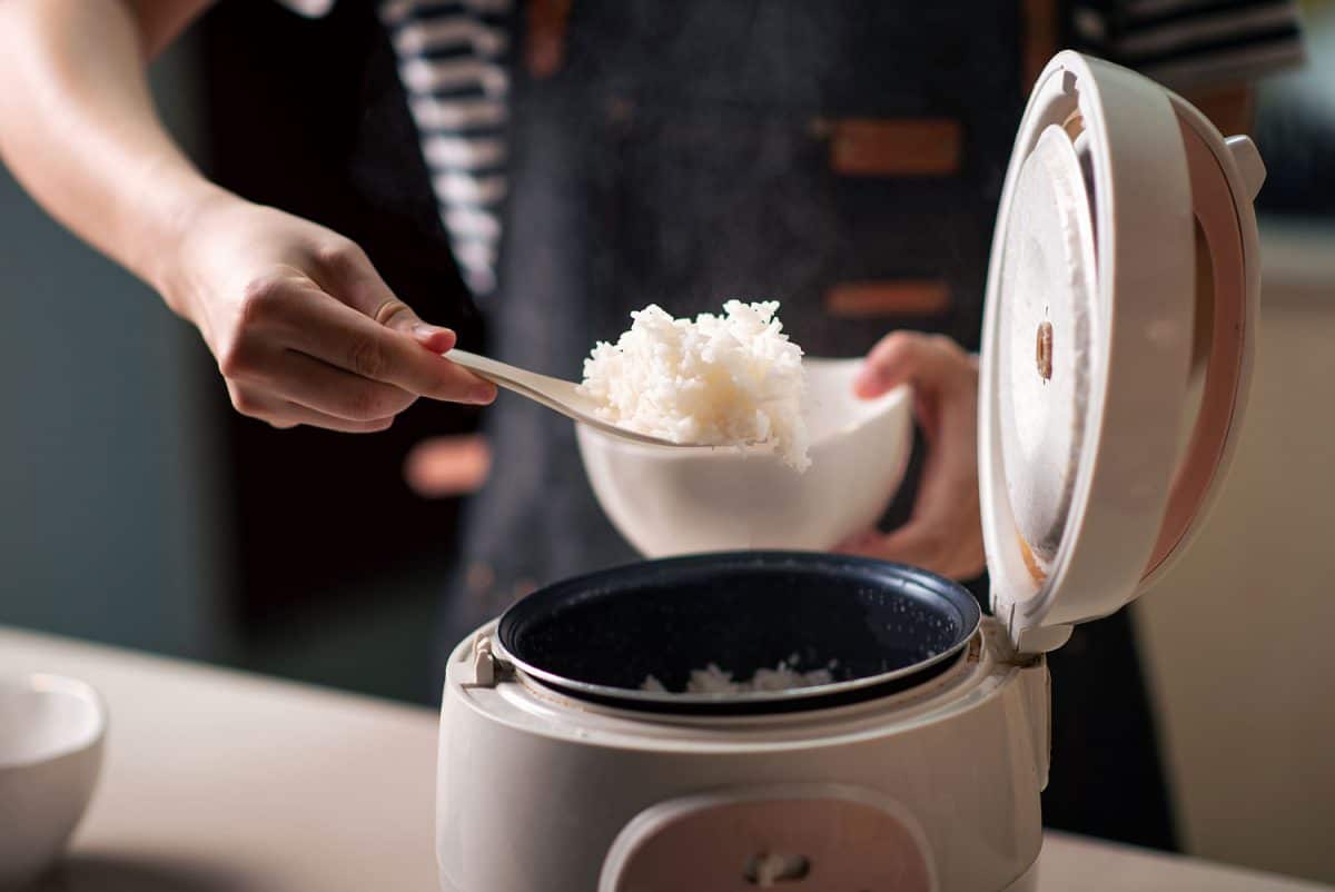 女人从电饭煲里拿出新鲜煮好的香喷喷的茉莉花米饭