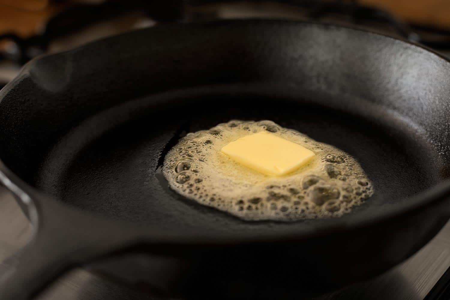 在黑色铸铁煎锅上融化的黄油块