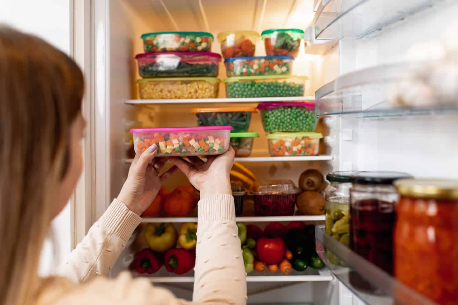 近距离拍摄的女子从冰箱中取出装有冷冻混合蔬菜的容器，同时看着相机。
