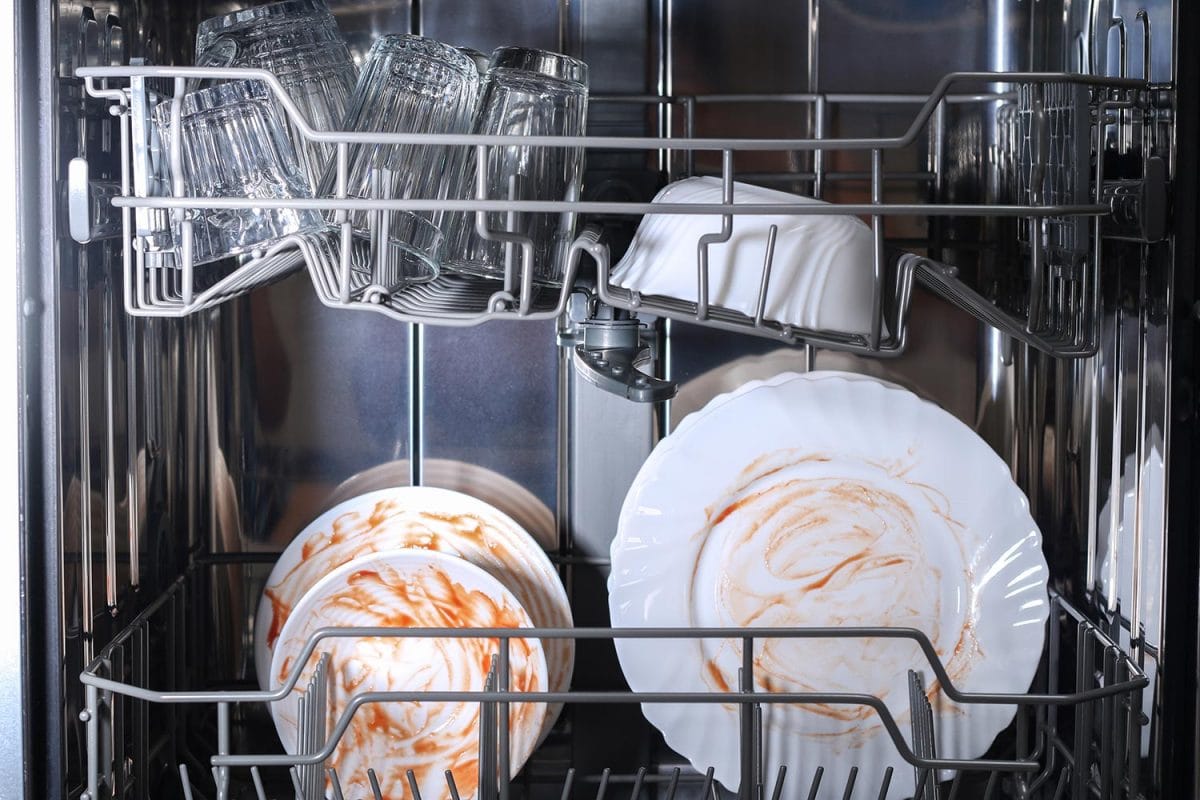 男人把脏盘子、盘子、勺子、叉子、餐具装进洗碗机托盘