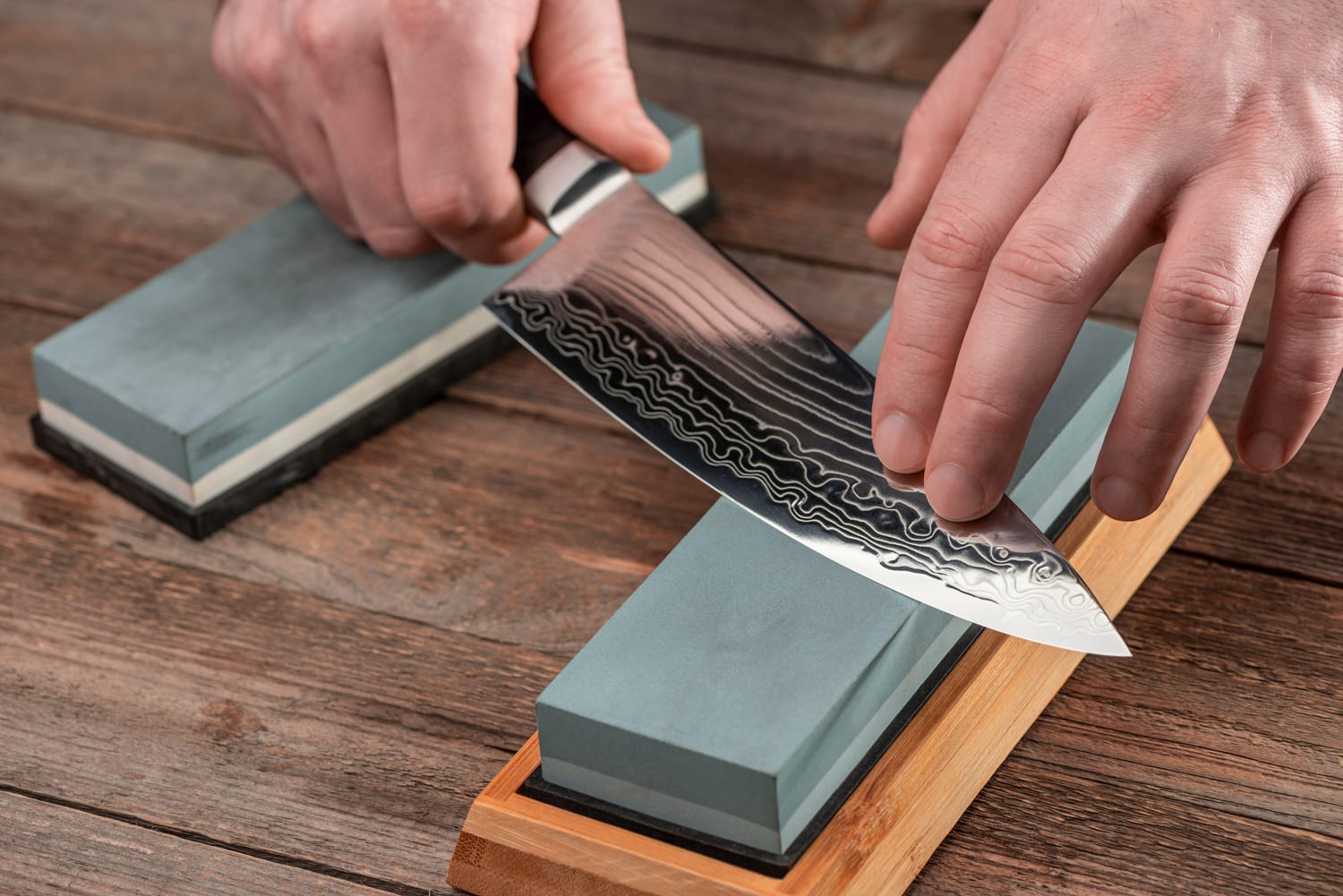 一名男子在质朴的木桌上用磨刀石磨砺一把龟户刀。