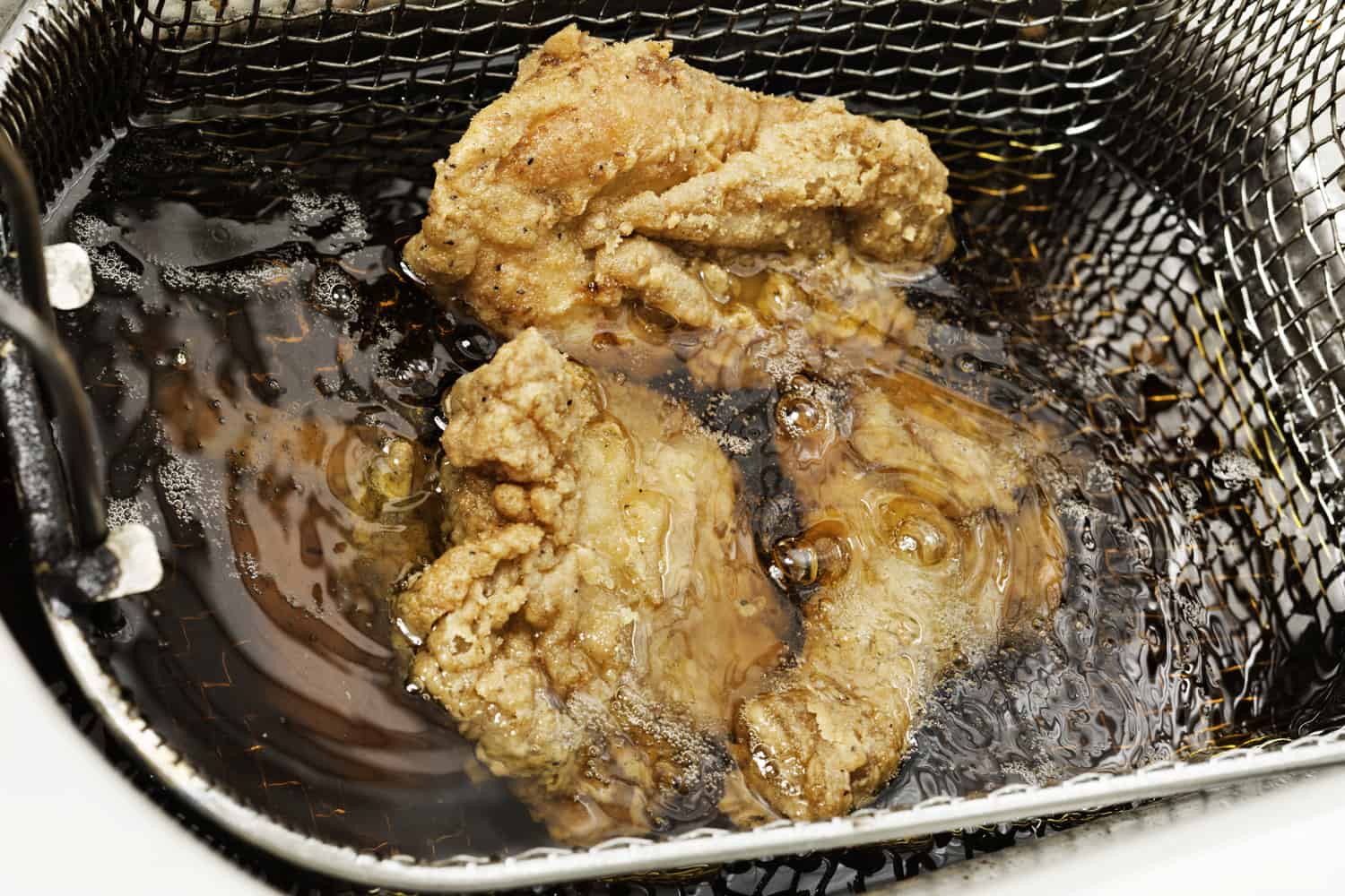 裹上面包屑的鸡肉块在热油里炸。它们被一个铁丝网篮子固定着。专注于油和上面的部分。
