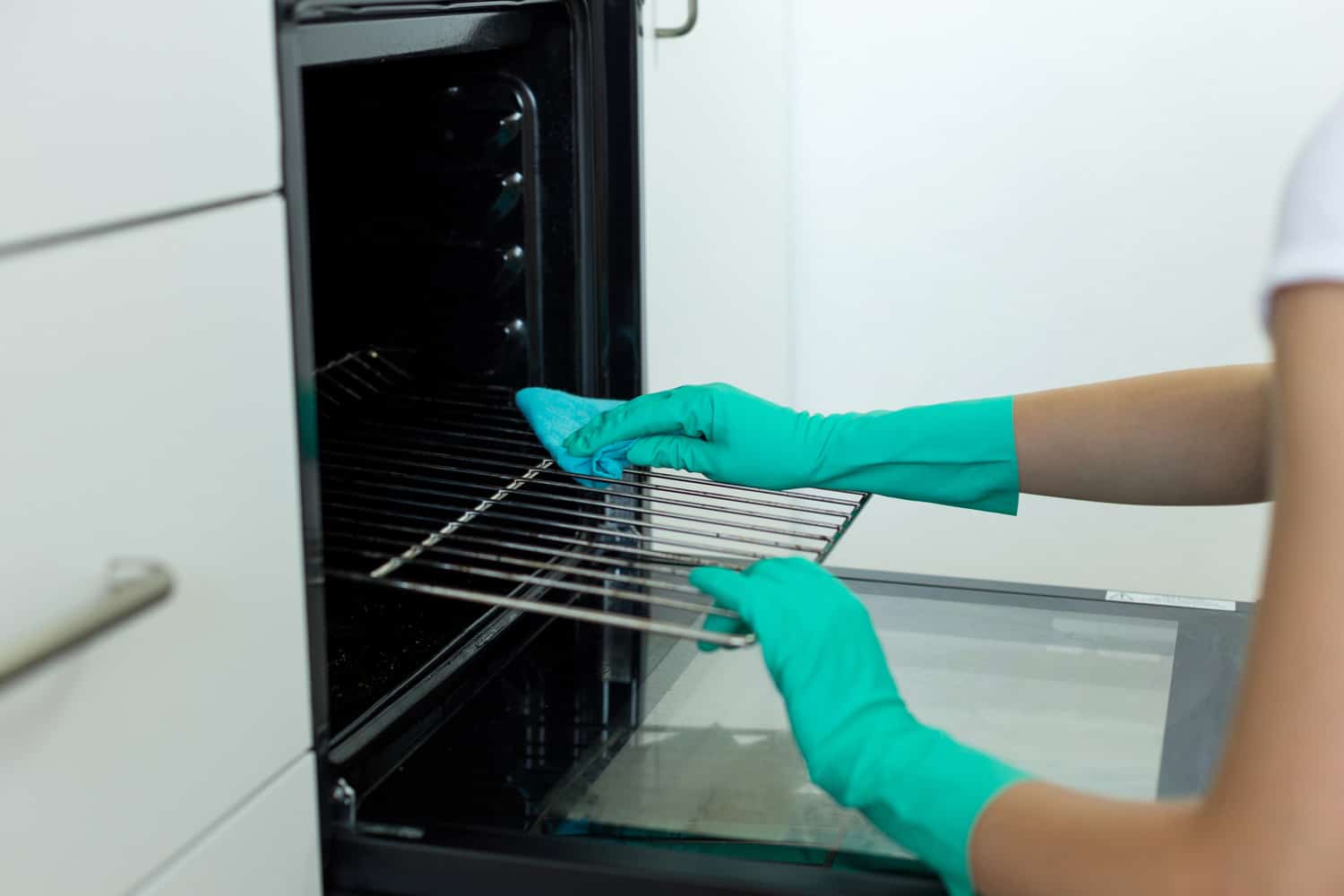 妇女手戴防护手套，用抹布清洗烤箱