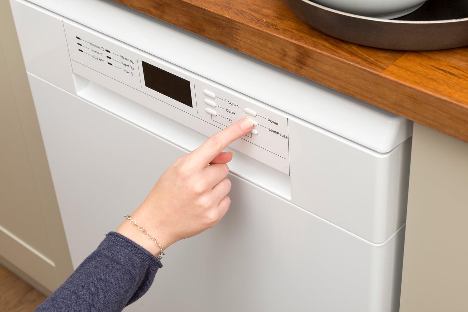 女人的手指按下洗碗机的“开始”按钮