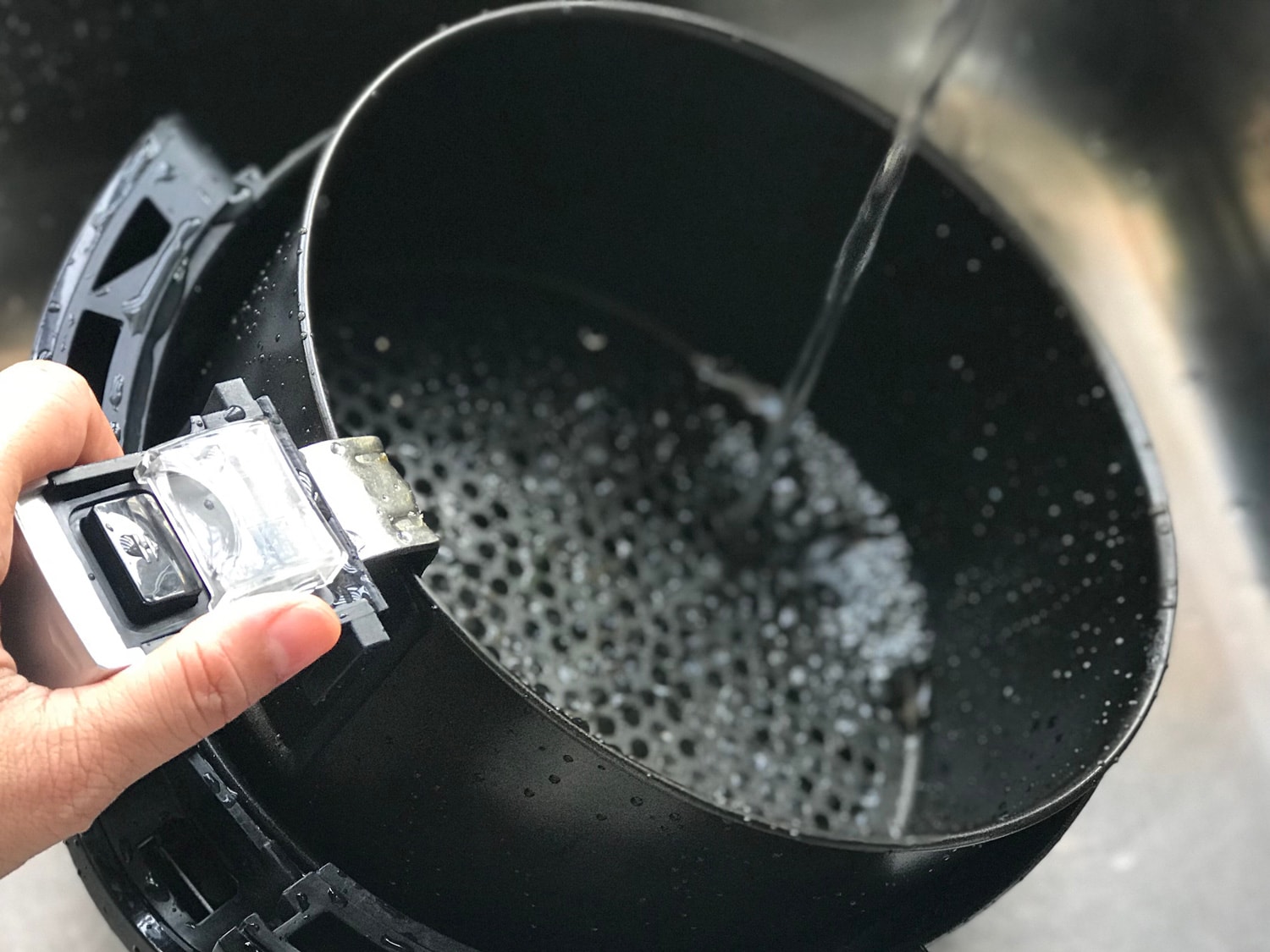 妇女的手拿着把手的空气炸锅的篮子清洗。