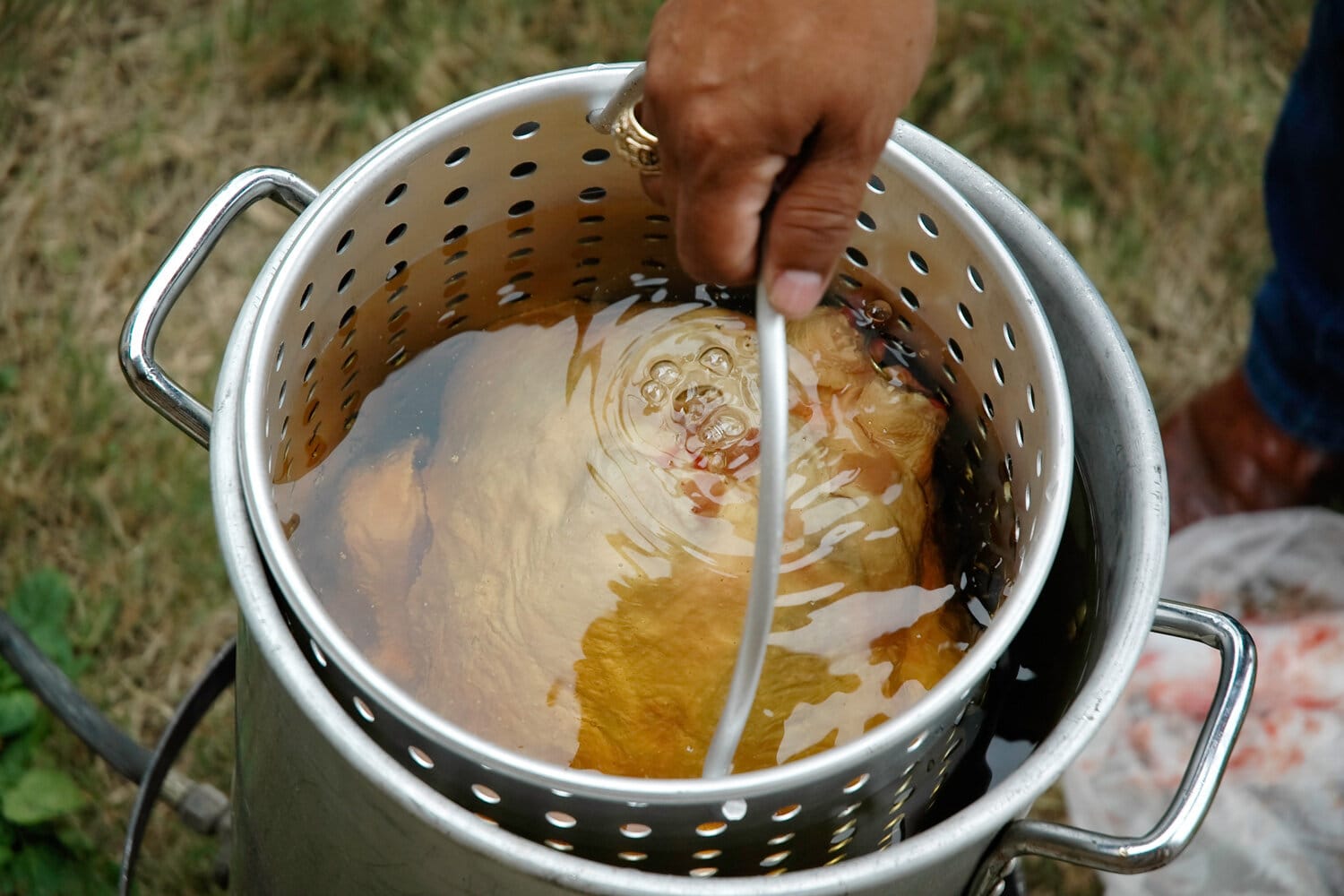 一只火鸡慢慢地放进装有热花生油的大锅里煎炸。