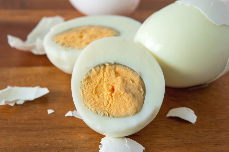 近一半割接煮坏煮鸡蛋木制板。周围的绿色黄色的鸡蛋在煮太久。煮鸡蛋高蛋白质饮食健康的零食。——多久煮鸡蛋(软、硬)