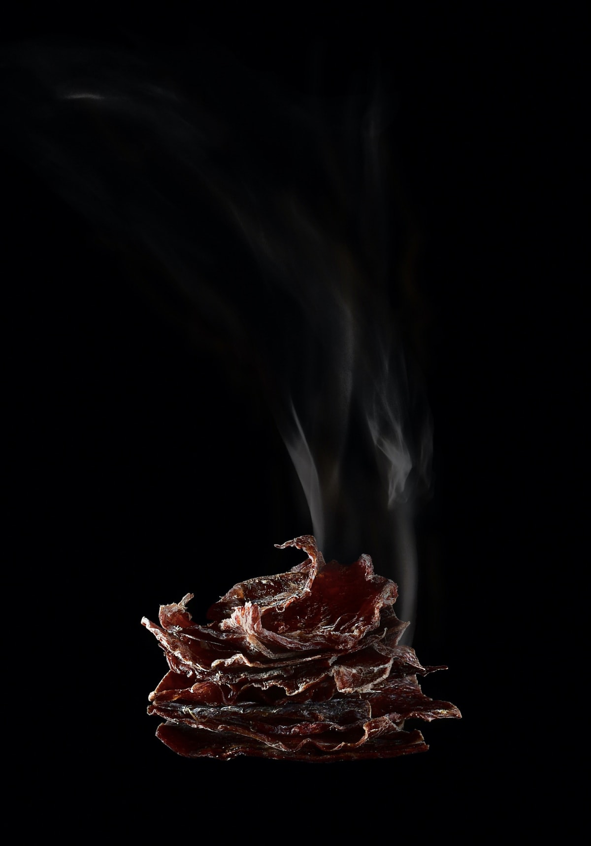 干鹿肉。与卷边薄木板,形状像一个金字塔,和一缕烟雾向上发出的火焰的形式,垂直隔离在一个黑色背景。
