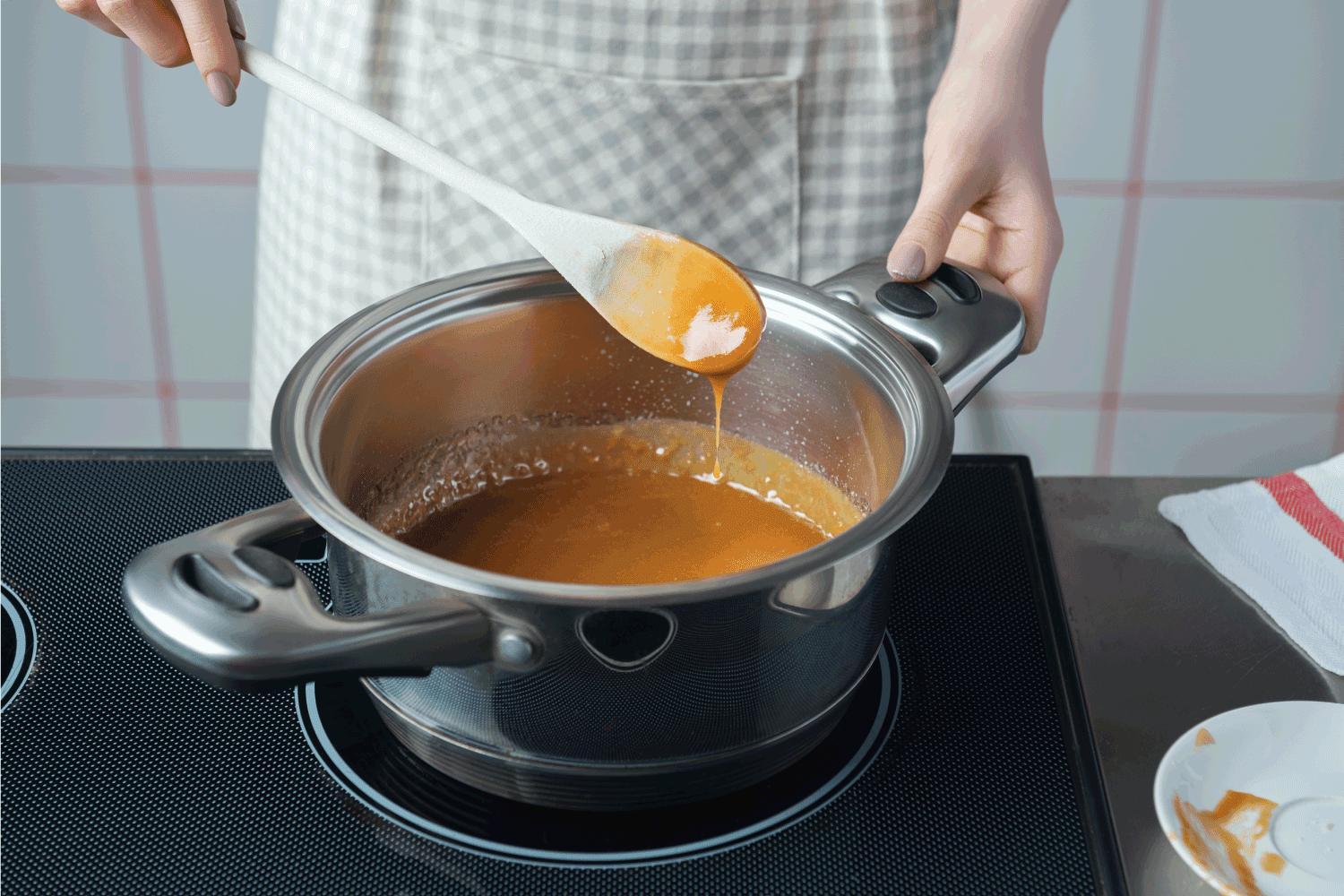 穿着格子围裙的女人拿着木勺在不锈钢锅里准备焦糖。