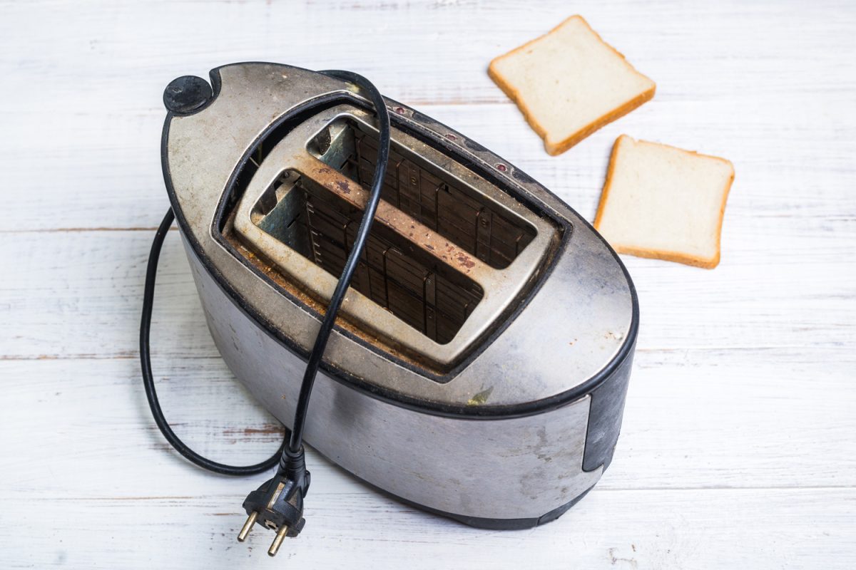 又脏又旧的烤面包机，白色的木质背景上放着面包。